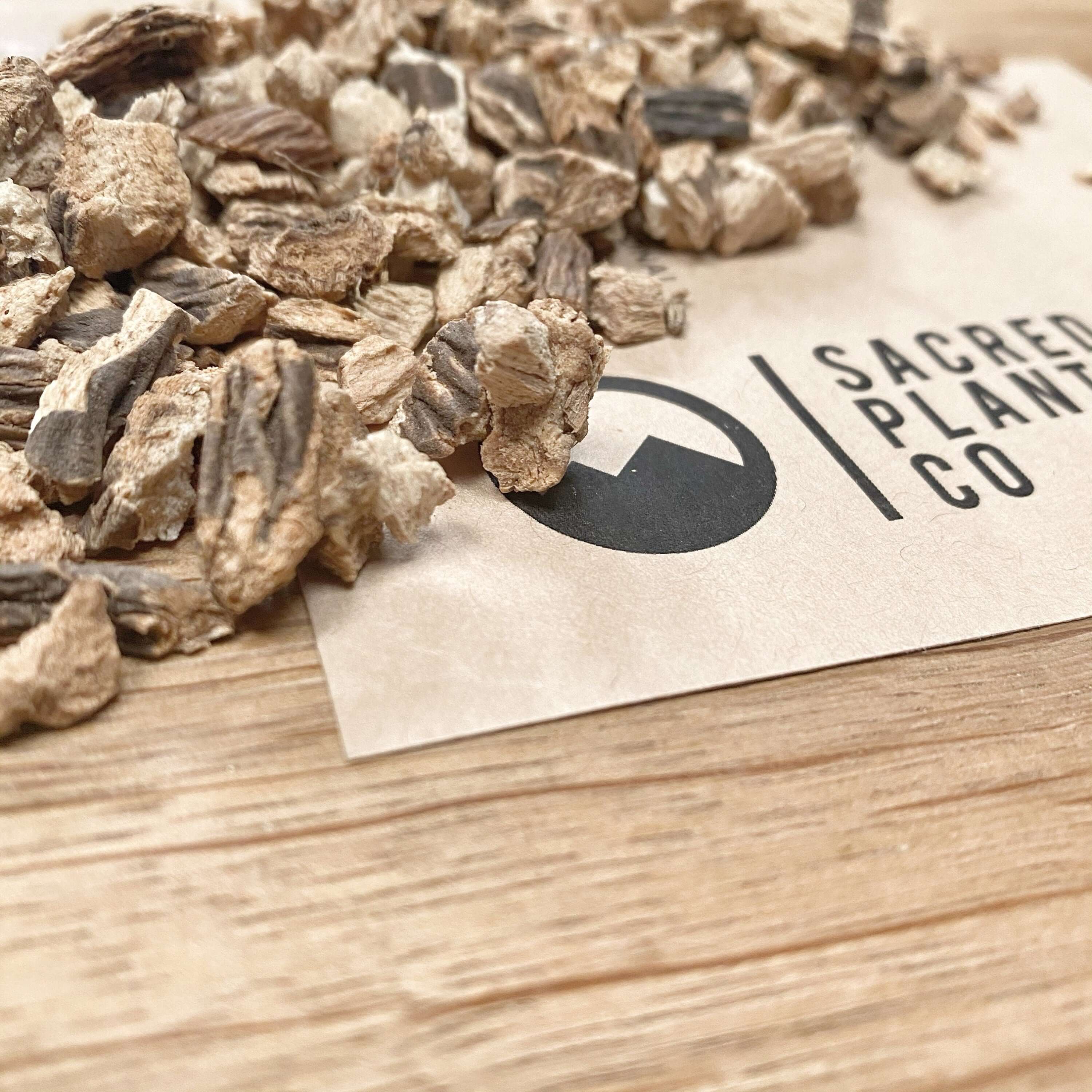 Gentian Root pieces scattered on top of Sacred Plant Co logo, close-up view highlighting the rough texture, natural hues, and high quality.