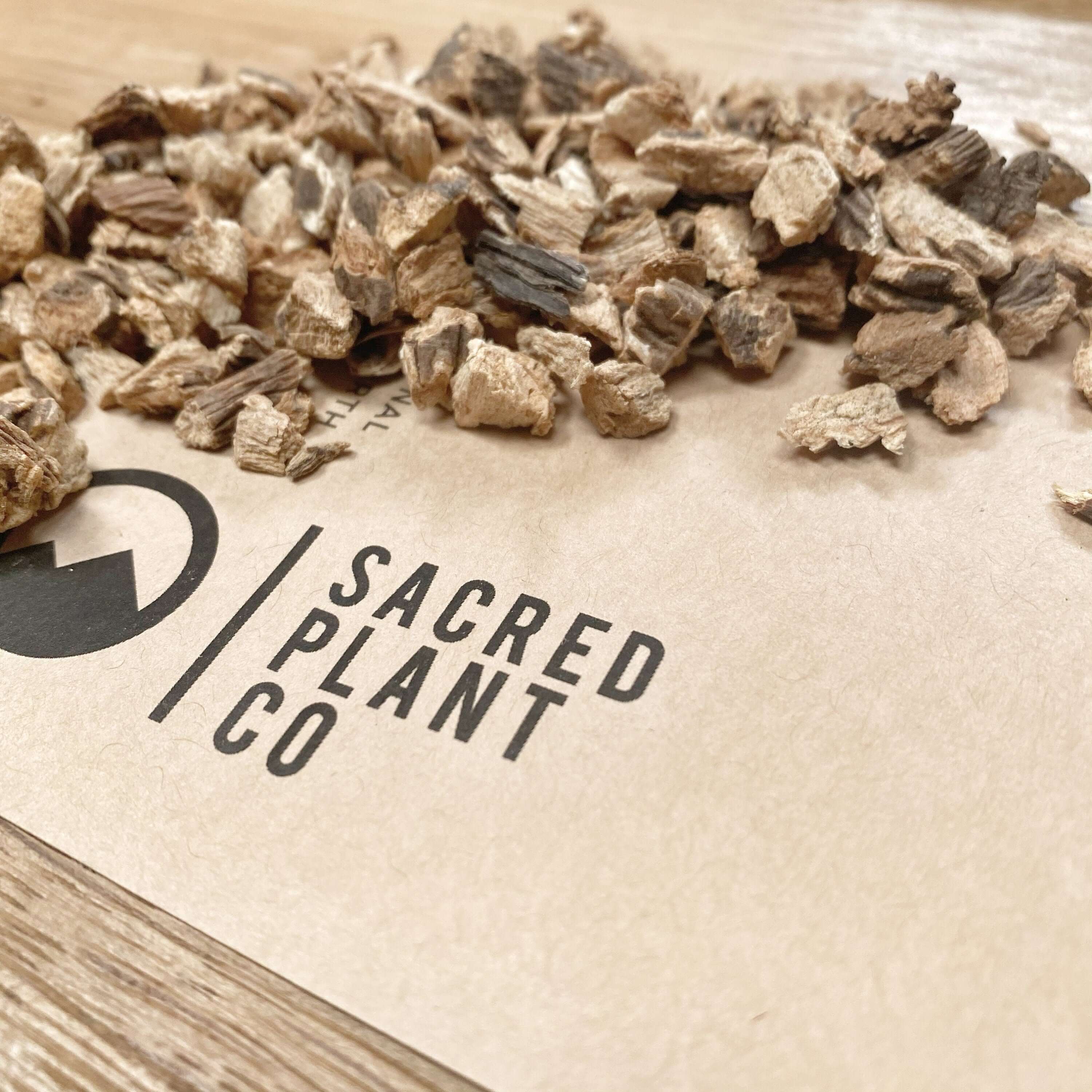 Close-up of organic Gentian Root pieces from Sacred Plant Co, showcasing detailed texture, earthy tones, and visible logo on a natural wood background.