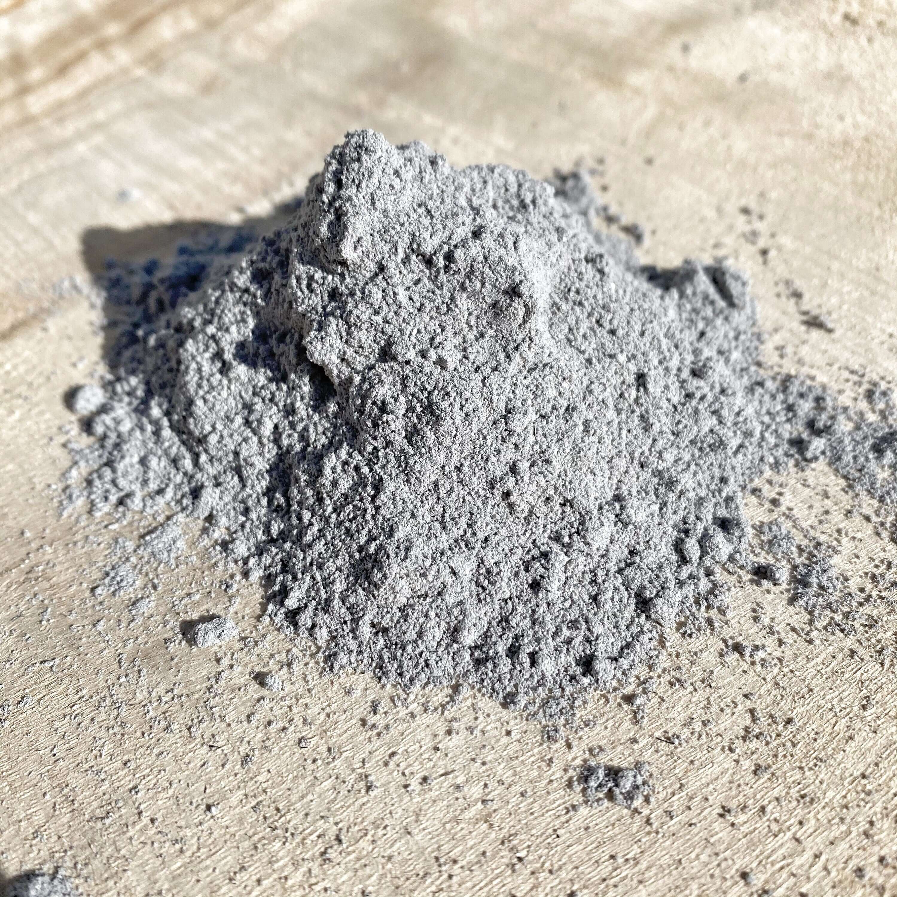 A mound of fine gray Vibhuti, also known as sacred Shiva ash, displayed on a textured beige background, used for spiritual practices and blessings.