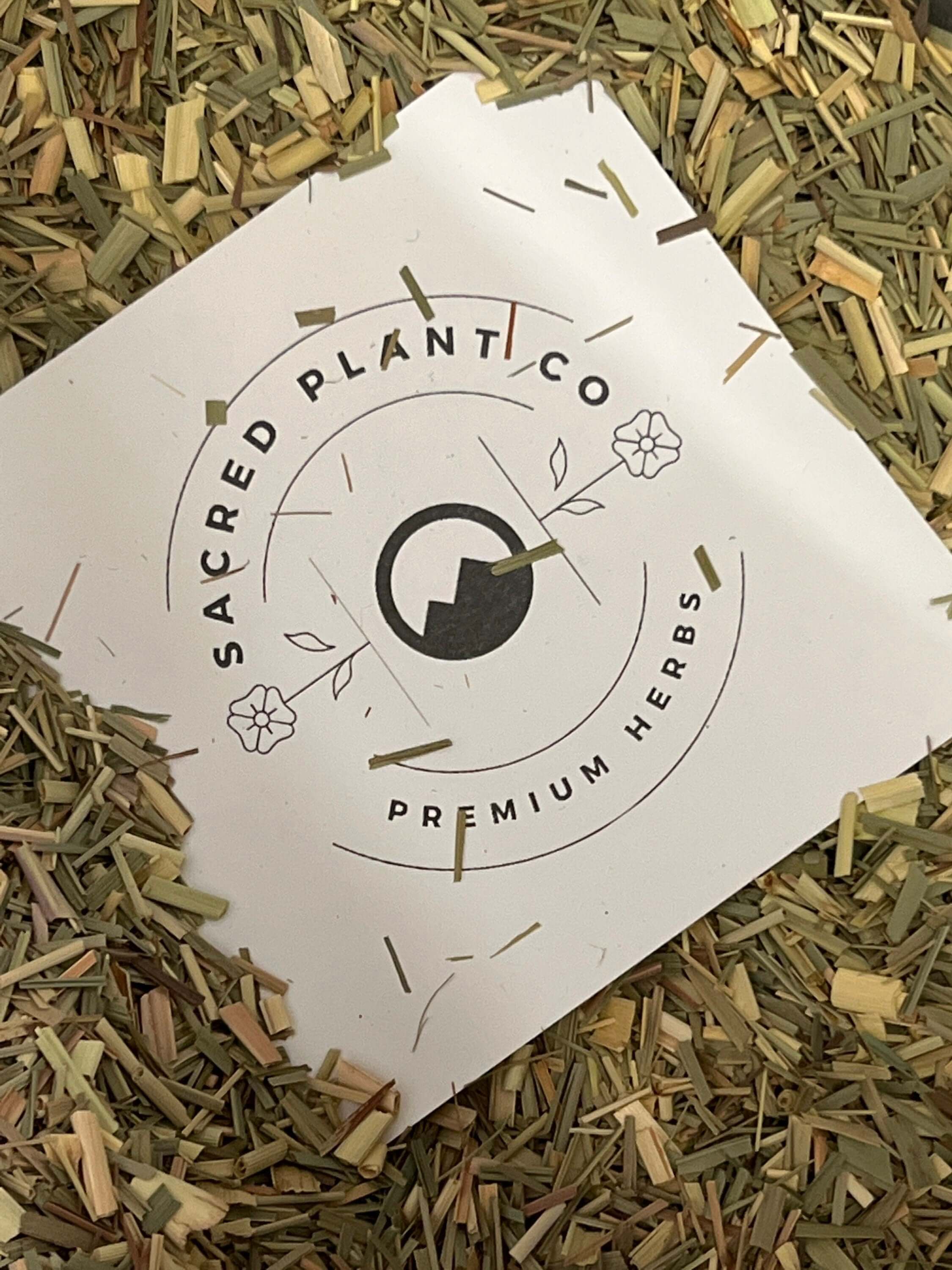 Finely cut Lemongrass from Sacred Plant Co, vibrant green and beige herb pieces surrounding a branded label, showcasing premium quality.