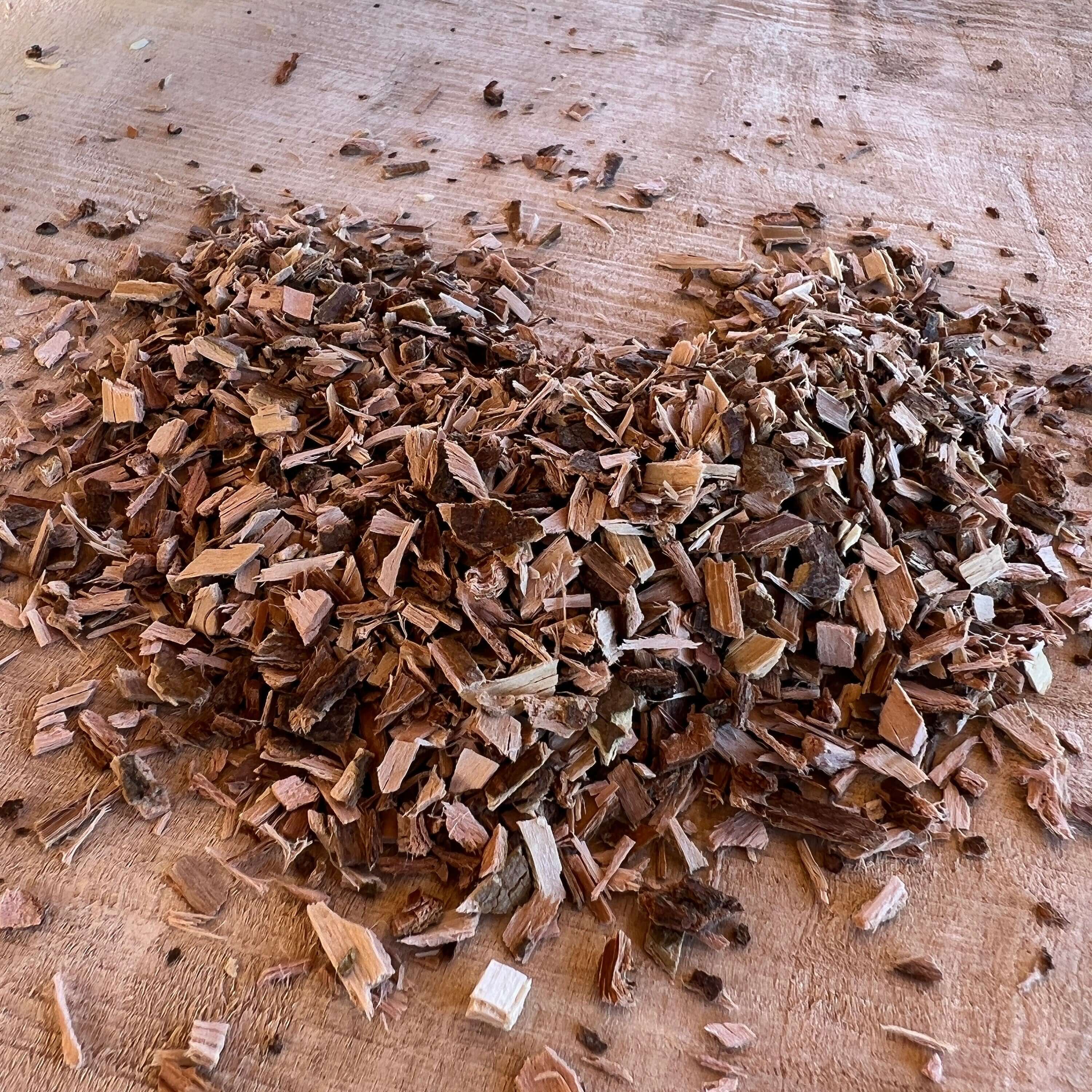 High-quality White Willow Bark pieces from Sacred Plant Co, cut into small, uniform chips, spread across a rustic wooden surface.