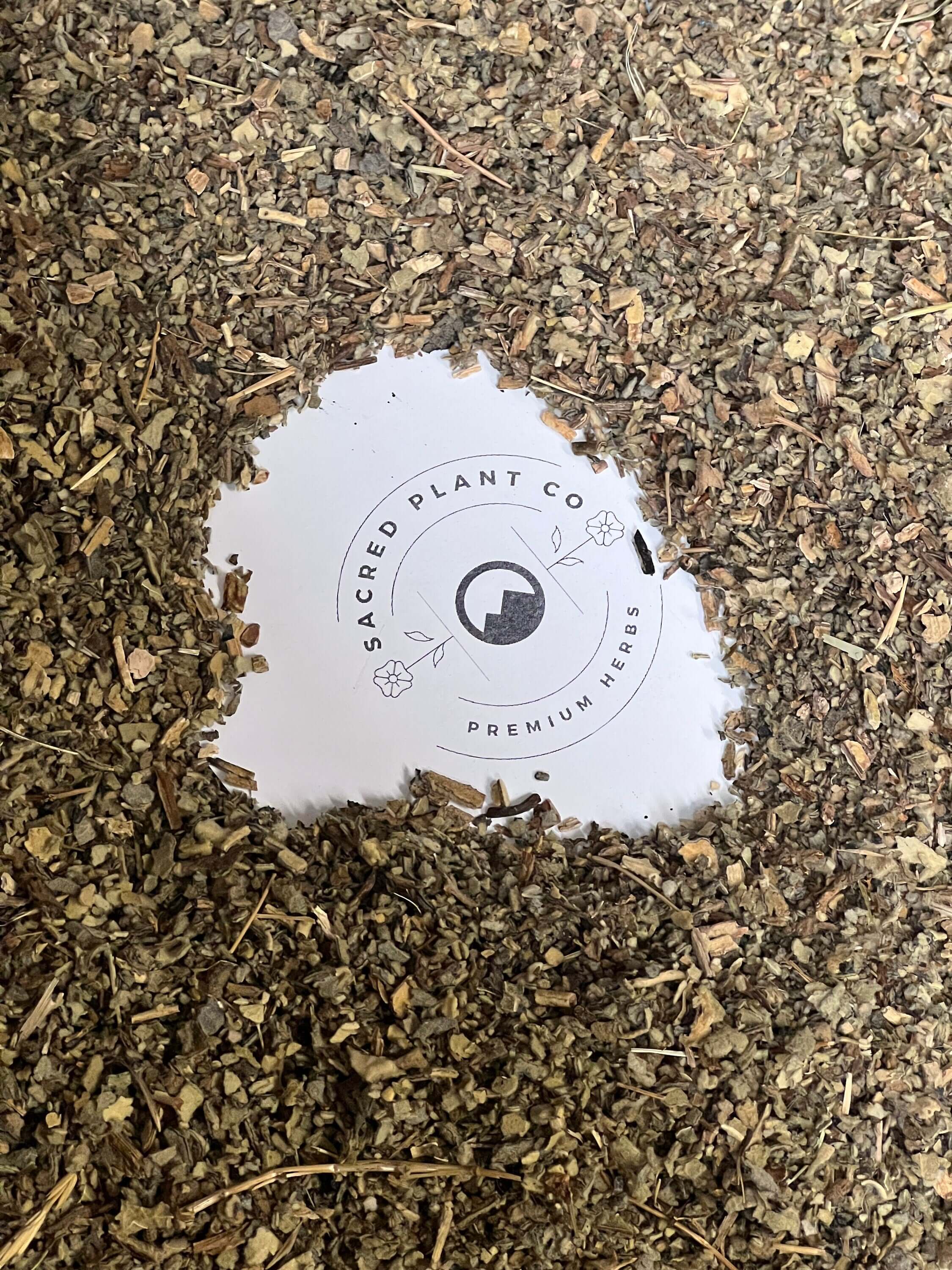 Sacred Plant Co’s logo surrounded by chopped Mullein Leaf herbs in earthy brown hues, showcasing superior quality herbal ingredients.