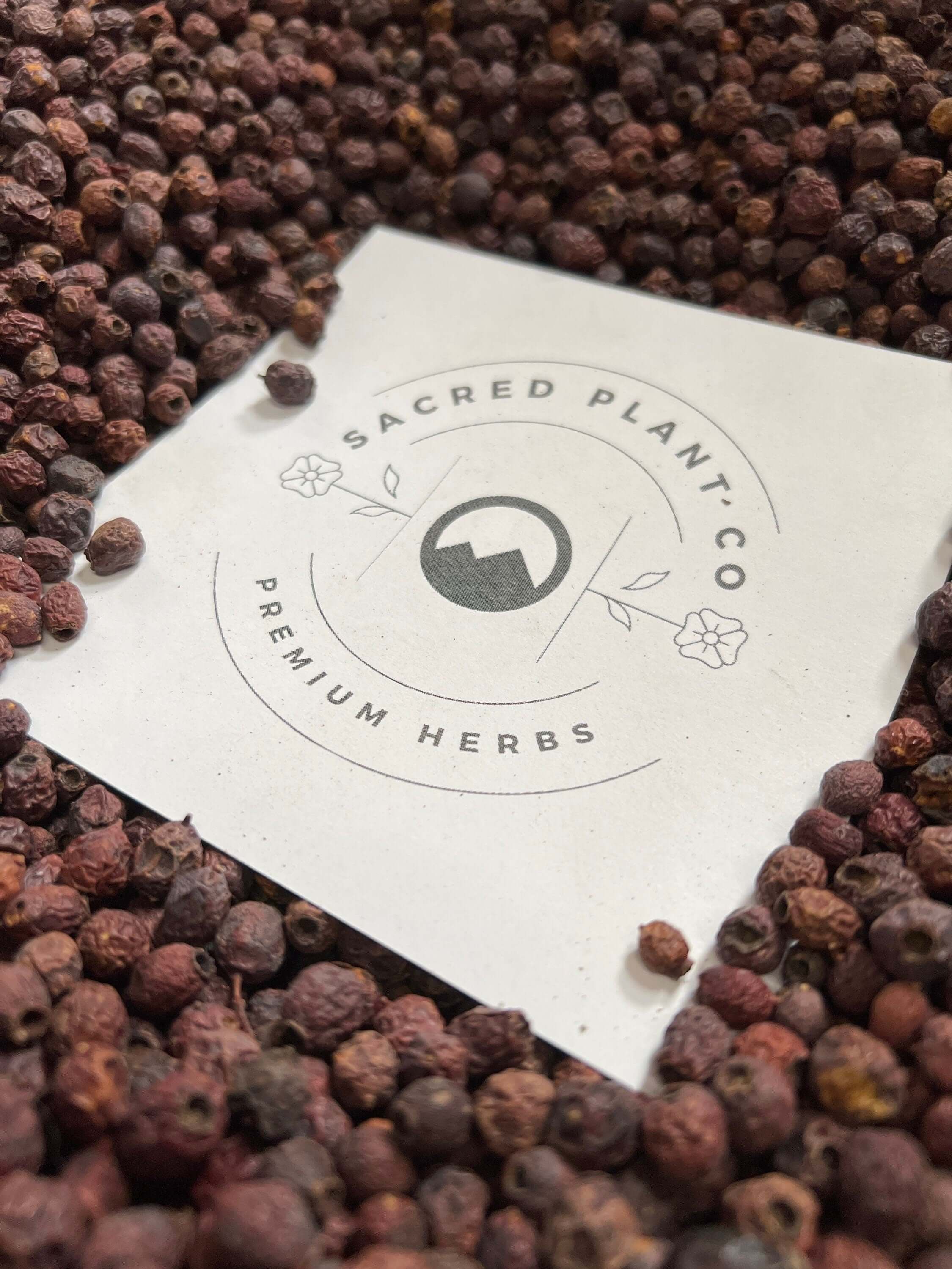Sacred Plant Co’s logo nestled in a bed of deep-hued Hawthorn Berries, showcasing the texture and superior quality of the product.