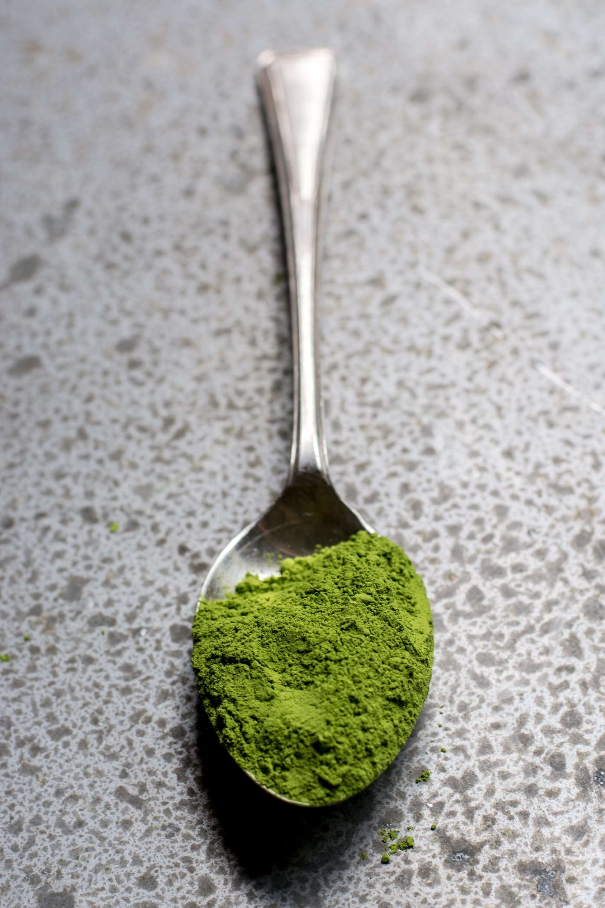 A spoonful of Sacred Plant Co Sasquatch Piss green powder on a textured surface, highlighting a fine and vibrant superfood blend.