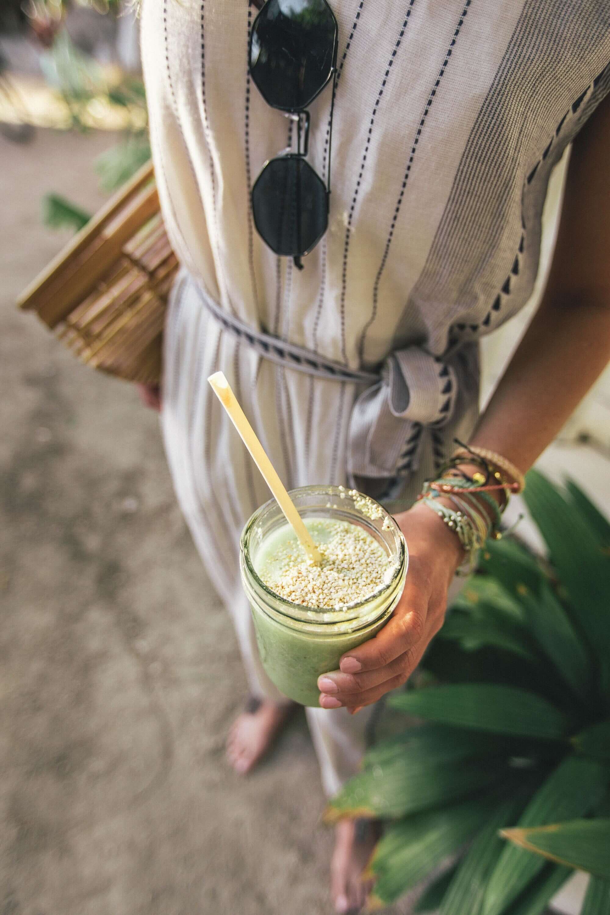 Healthy Sasquatch Piss green powder smoothie in hand with seed toppings, casual summer attire and accessories, highlighting a fresh lifestyle at Sacred Plant Co.