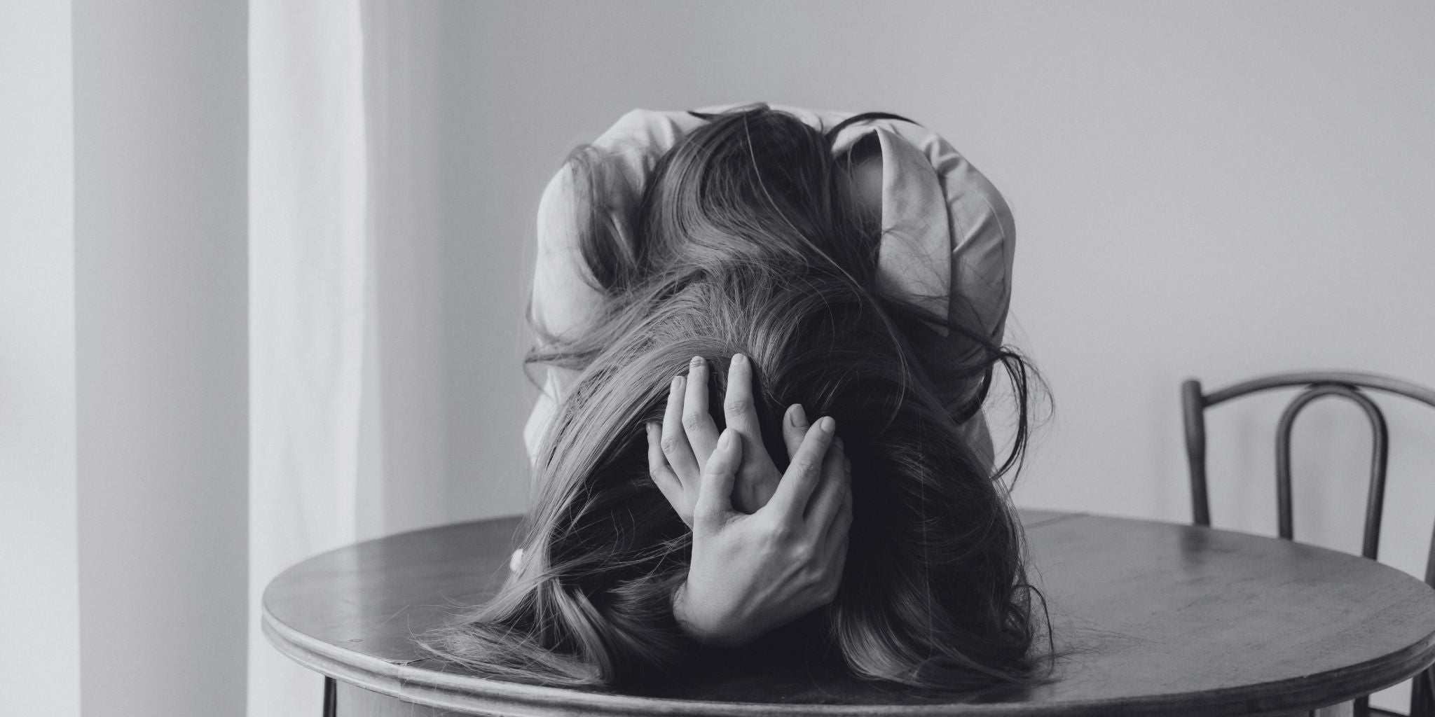 Person overwhelmed with anxiety, head resting on a table, symbolizing stress and mental health challenges. Focus on natural anxiety relief solutions.