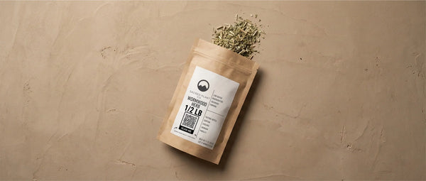 High-angle view of dried Artemisia absinthium spilling from packaging, highlighting the raw botanical ingredient used in absinthe and medicinal teas.