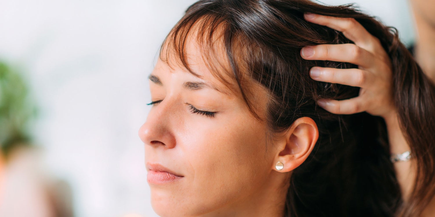 Close-up of a woman with her eyes closed, receiving a gentle scalp massage, symbolizing relaxation and natural hair growth practices. The soothing environment emphasizes self-care, wellness, and natural approaches to boost hair health.