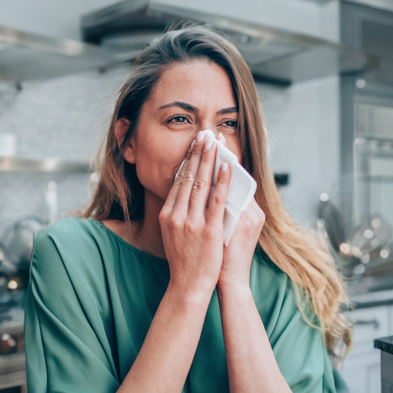 A woman in a green blouse holding a tissue to her nose, dealing with allergy symptoms, with a look of relief or hope, suggesting the potential benefits of natural herbal remedies for allergies.