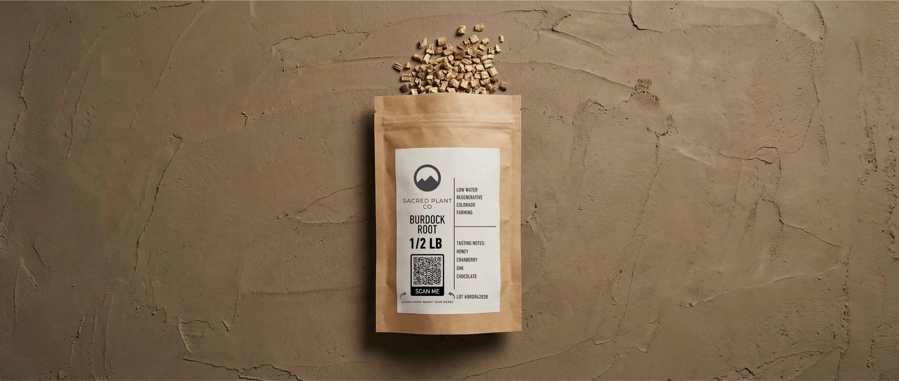 Dried Burdock root pieces spilling from Sacred Plant Co paper packaging onto a textured, earth-tone clay background.