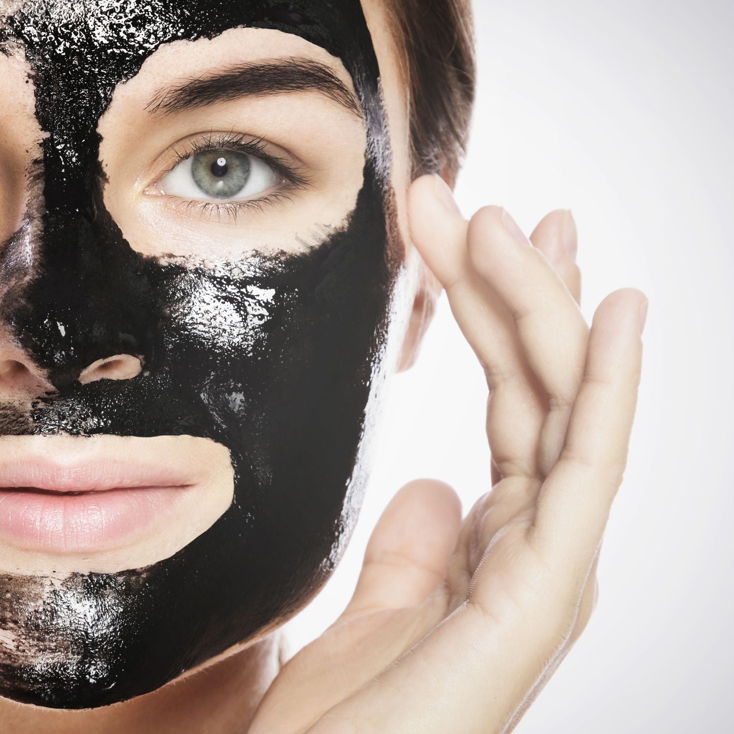 A woman peeling off a black Ayurvedic face mask from one side of her face, highlighting the smooth, clear skin underneath, demonstrating the cleansing and rejuvenating effects of the mask