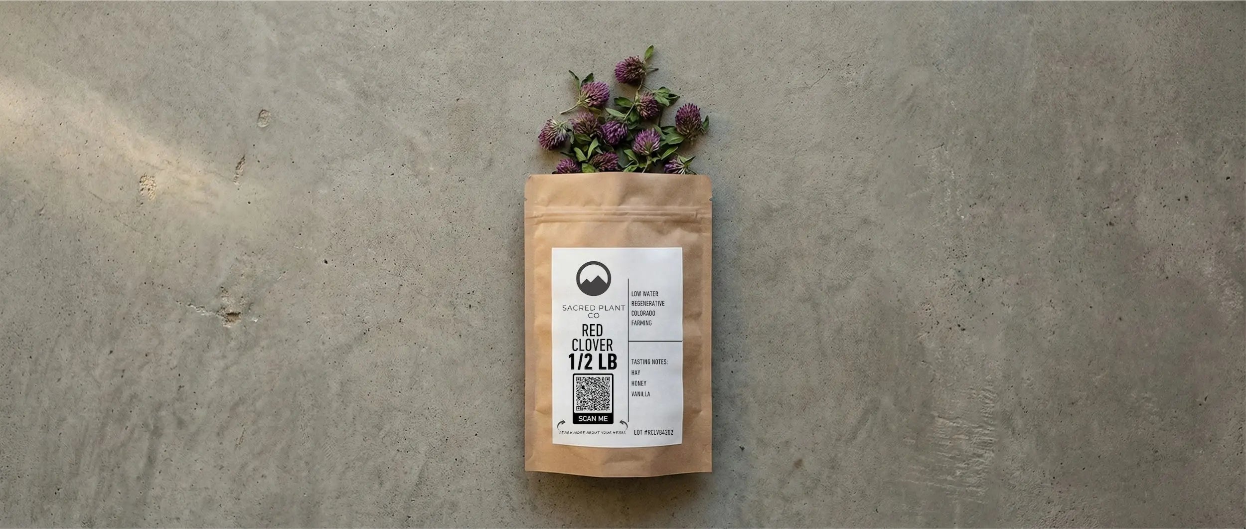Sacred Plant Co sustainable 1/2 LB bag of bulk Red Clover blossoms on a textured grey surface with loose dried flowers.