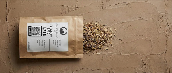Sacred Plant Co Uncaria tomentosa packaging displayed with raw dried bark chips, illustrating the texture of wild-harvested Amazonian medicine.