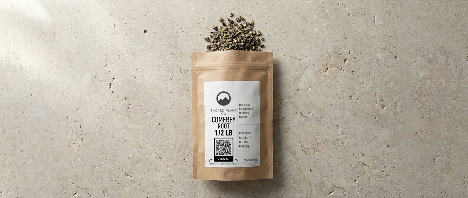 A 1/2 lb kraft pouch of Sacred Plant Co dried comfrey root spilling onto a textured stone surface. The regeneratively farmed Symphytum officinale is a restorative herb rich in allantoin, used externally to support natural bone healing.