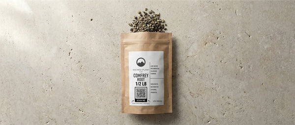 A 1/2 lb kraft pouch of Sacred Plant Co dried comfrey root spilling onto a textured stone surface. The regeneratively farmed Symphytum officinale is a restorative herb rich in allantoin, used externally to support natural bone healing.