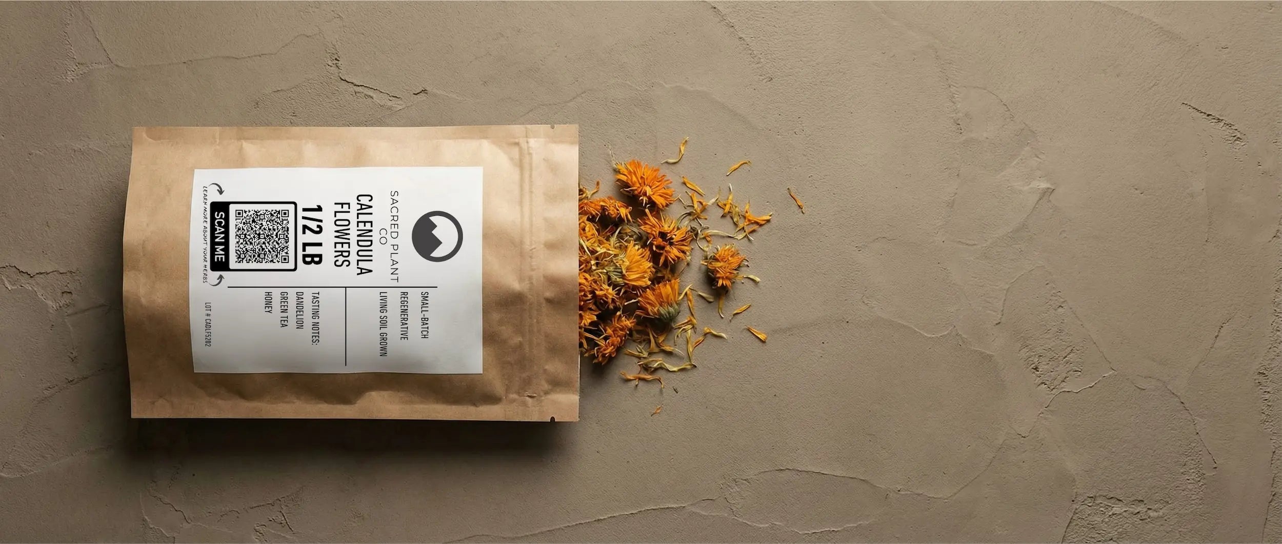 A biodegradable bag of Sacred Plant Co dried calendula flowers spills vibrant orange resinous petals onto a textured stone surface.