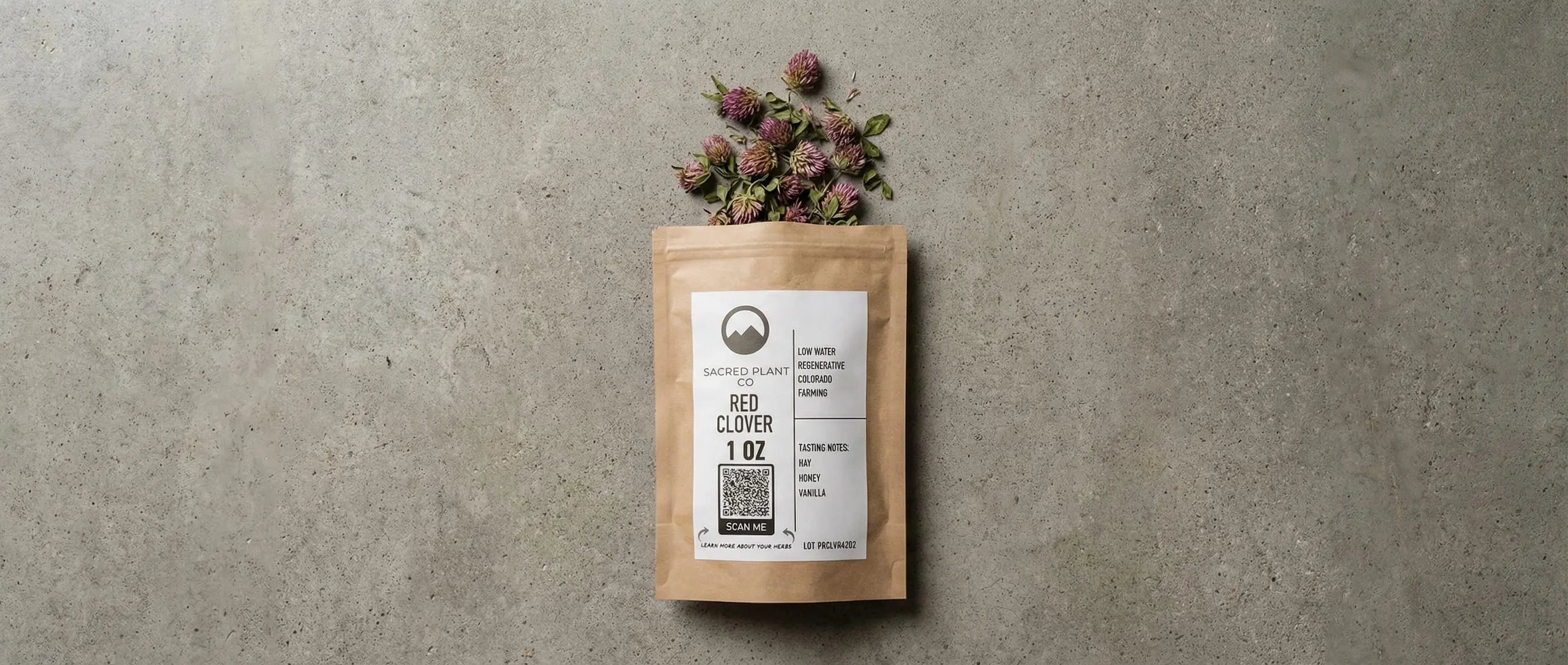 Top-down view of Sacred Plant Co Red Clover 1oz bag with dried pink and purple blossoms spilling onto a grey stone surface.