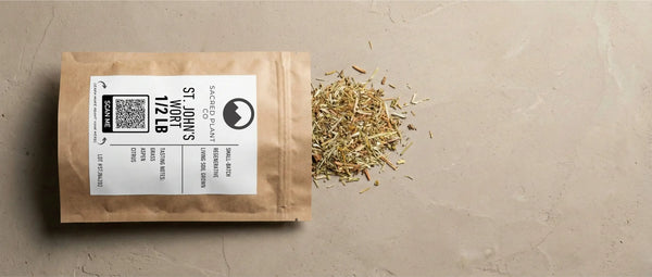 Premium Sacred Plant Co bulk St. John's Wort (1/2 LB) grown in regenerative living soil biology, open kraft paper pouch with dried aerial parts spilling out, featuring a scan me QR code and tasting notes on textured, earth-toned ground.