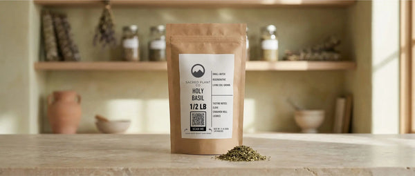 A 1/2 LB kraft paper pouch of Sacred Plant Co regeneratively grown Holy Basil sitting on a stone countertop. A small pile of the dried, loose-leaf herb rests directly in front of the bag.