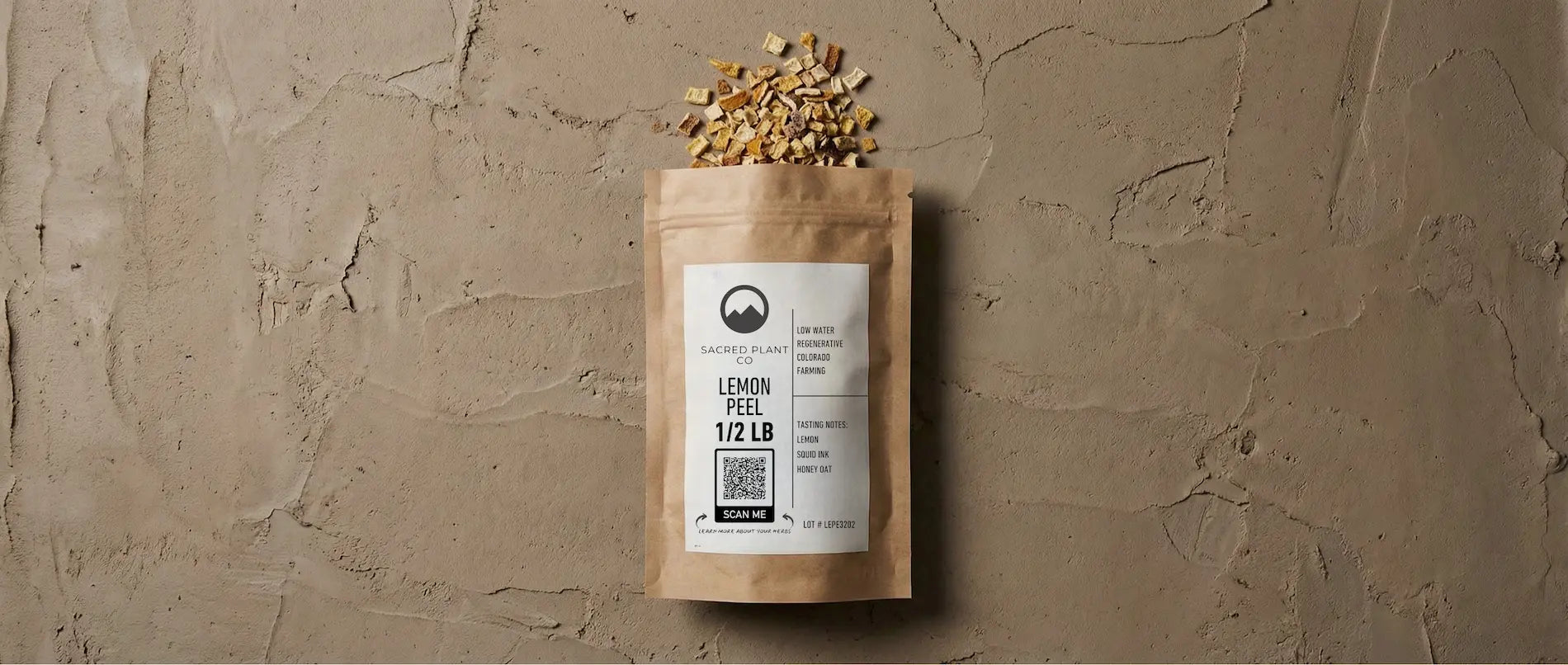 Minimalist editorial photography of a paper herb bag resting on a raw, hand-troweled earthen background. The image features high-contrast textures of dried botanical lemon peel against matte stone, evoking a grounded, modern apothecary aesthetic.