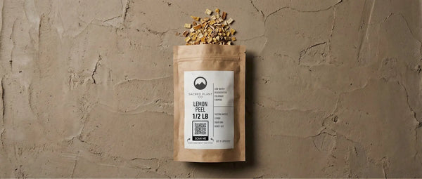 Minimalist editorial photography of a paper herb bag resting on a raw, hand-troweled earthen background. The image features high-contrast textures of dried botanical lemon peel against matte stone, evoking a grounded, modern apothecary aesthetic.