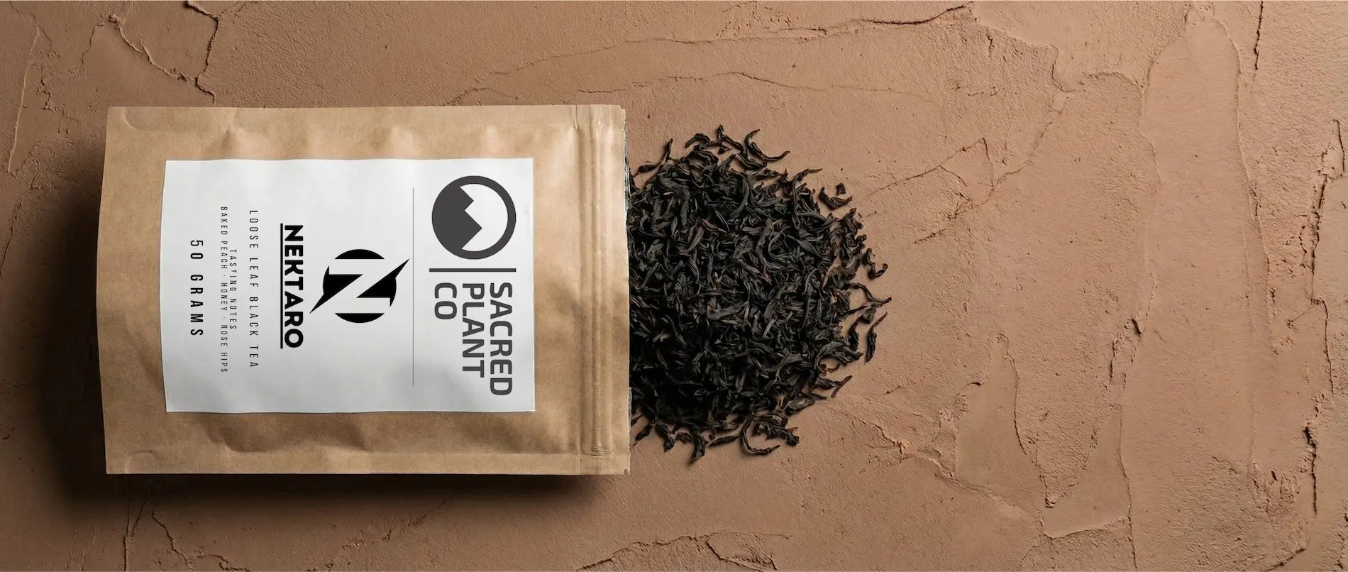 Sacred Plant Co Nektaro kraft bag lying next to a pile of dark, twisted Flowery Orange Pekoe loose leaf tea.