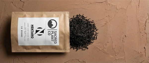Sacred Plant Co Nektaro kraft bag lying next to a pile of dark, twisted Flowery Orange Pekoe loose leaf tea.
