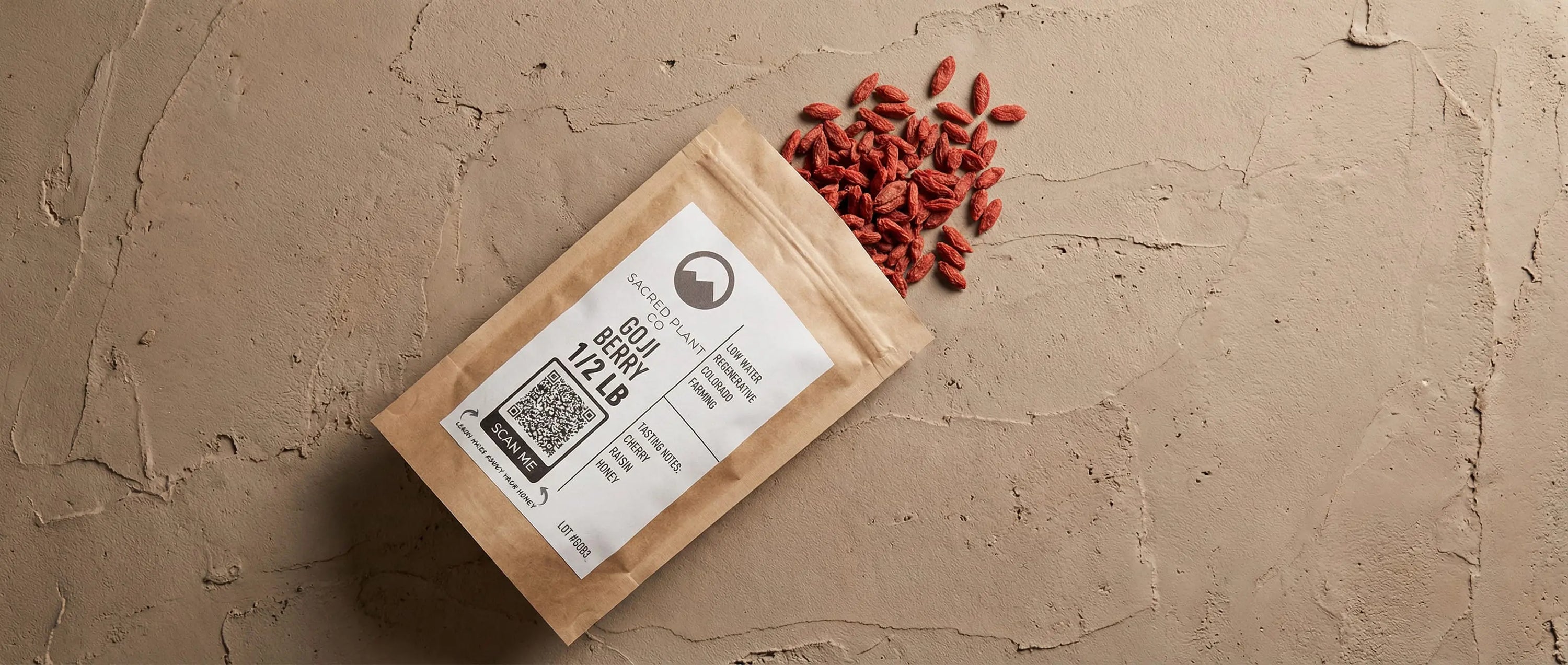 High-angle view of deep red dried goji berries spilling from a kraft paper bag onto a textured, earthy surface.