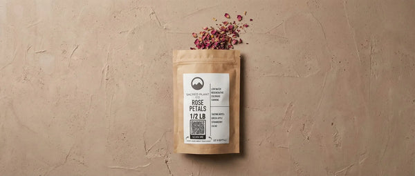 Overhead view of Sacred Plant Co dried rose petals spilling from kraft packaging onto a textured beige surface.