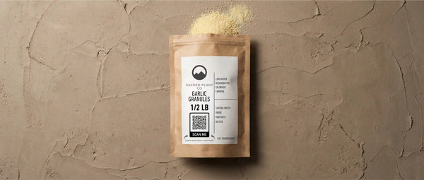 Top-down view of Sacred Plant Co Garlic Granules 1/2 LB kraft package on a textured earth-tone surface, with spilled golden granules showing texture and grind consistency.