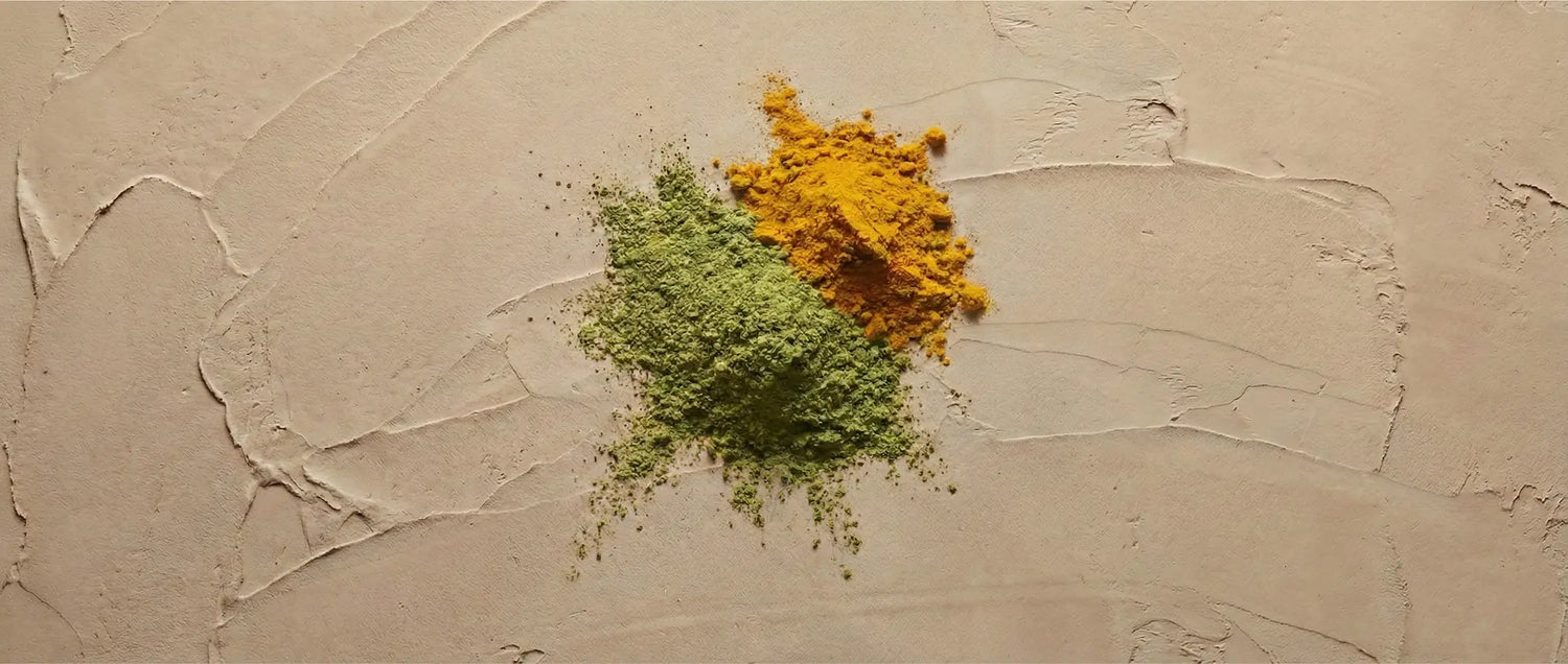 Overhead view of vibrant turmeric powder and green herbal powder on a textured, natural earth background, symbolizing regenerative herbs for skin health.