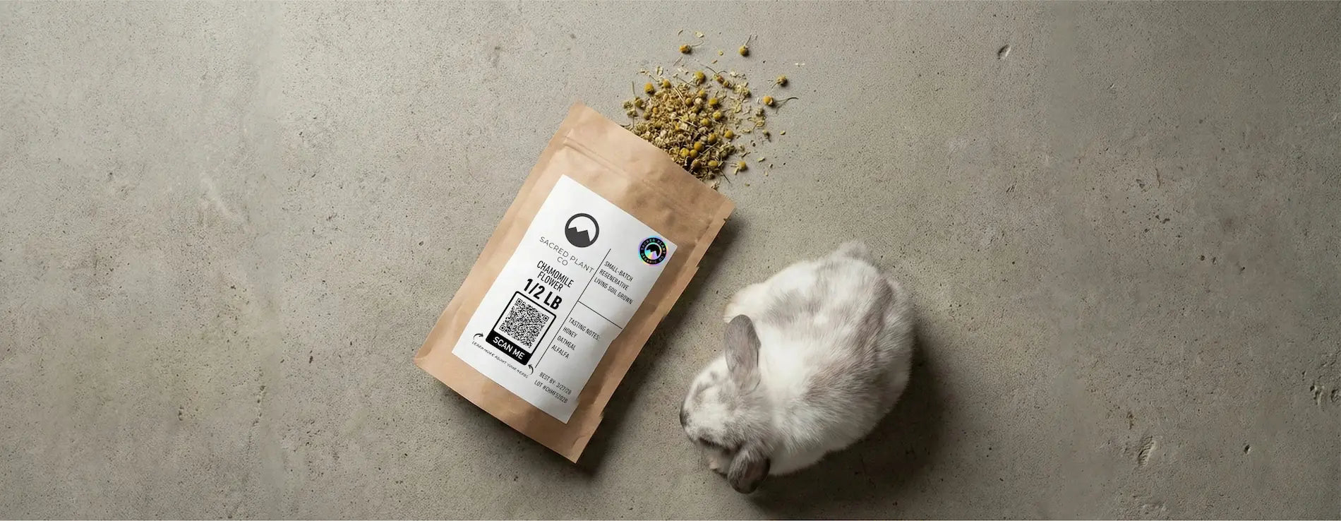 Overhead view of a brown kraft paper bag with a white label spilling dried chamomile flowers next to a small rabbit.
