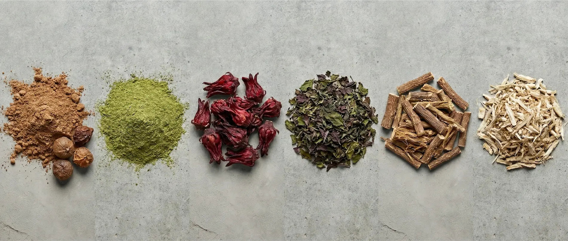 Top-down panoramic view of raw Ayurvedic hair ingredients including Amla powder, dried Hibiscus flowers, and Licorice root arranged on stone.
