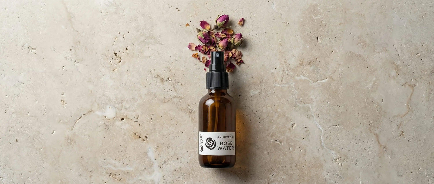 Top-down view of a rose water bottle on stone, with dried rose petals arranged to look like a spray burst from the nozzle.