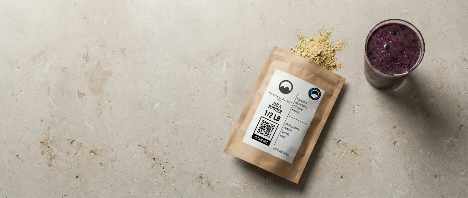 A 1/2 lb bag of Sacred Plant Co Amla Powder sitting on a stone surface next to a finished purple berry smoothie glass.