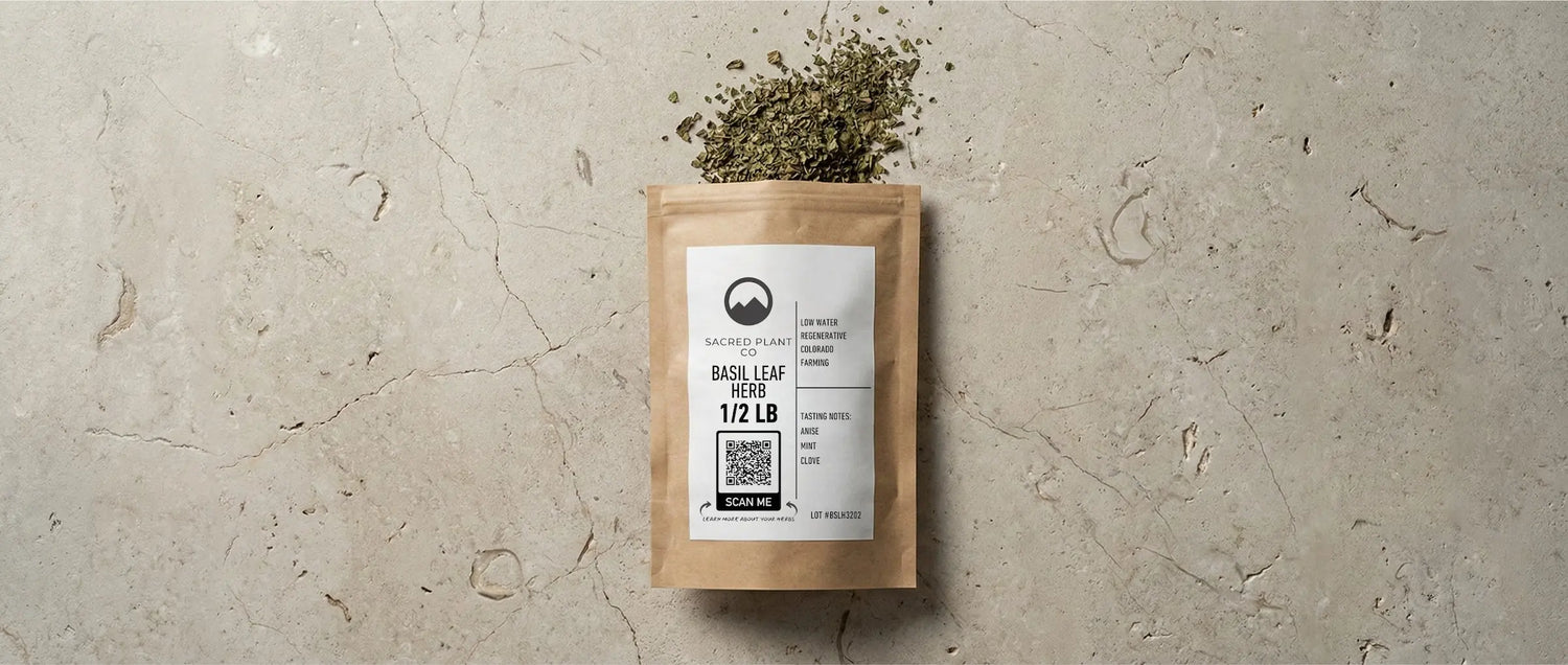 Sacred Plant Co package of dried Basil Leaf Herb showing the label details, QR code, and high-quality cut and sifted green leaves on a stone surface.