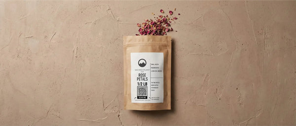 A kraft paper bag of Sacred Plant Co dried rose petals spilling onto a textured surface, illustrating natural herbs used to manifest dreams and attract abundance.