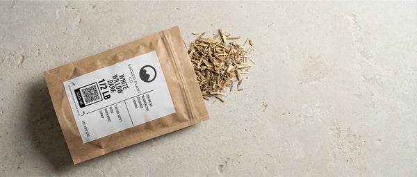 Sacred Plant Co sustainable paper packaging labeled White Willow Bark 1/2 LB, with dried cut and sifted bark spilling onto a stone surface.