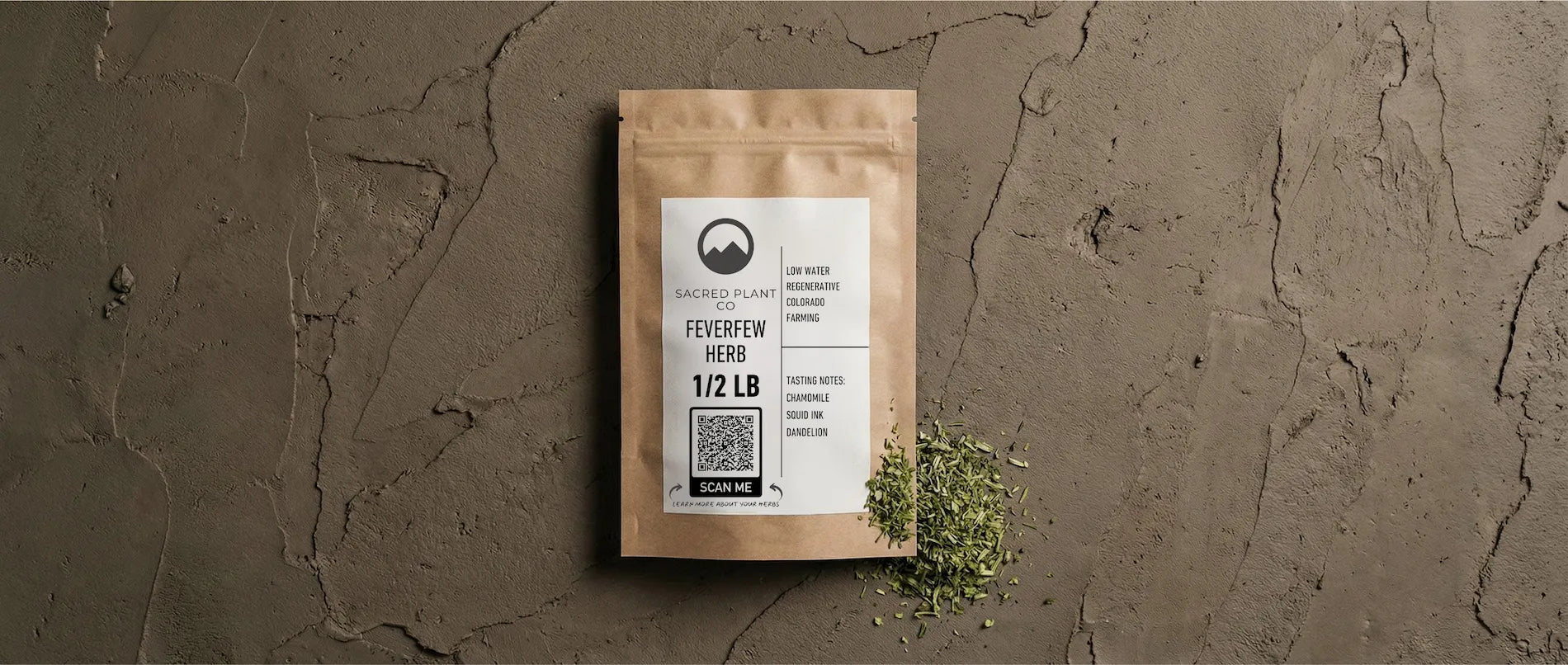 A kraft paper package of Sacred Plant Co Feverfew Herb (1/2 LB) sitting on an earthy textured surface, with spilled dried green herb showing leaf cut consistency and a scannable QR code for transparency.