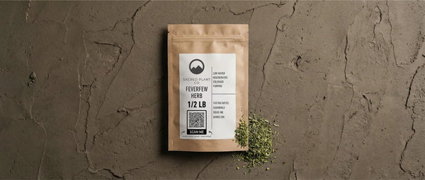 A kraft paper package of Sacred Plant Co Feverfew Herb (1/2 LB) sitting on an earthy textured surface, with spilled dried green herb showing leaf cut consistency and a scannable QR code for transparency.