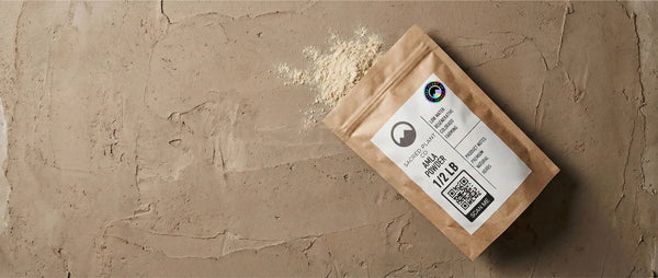 A bag of Sacred Plant Co Amla Powder spilled on a textured earth surface, showing the fine grind and light tan color.