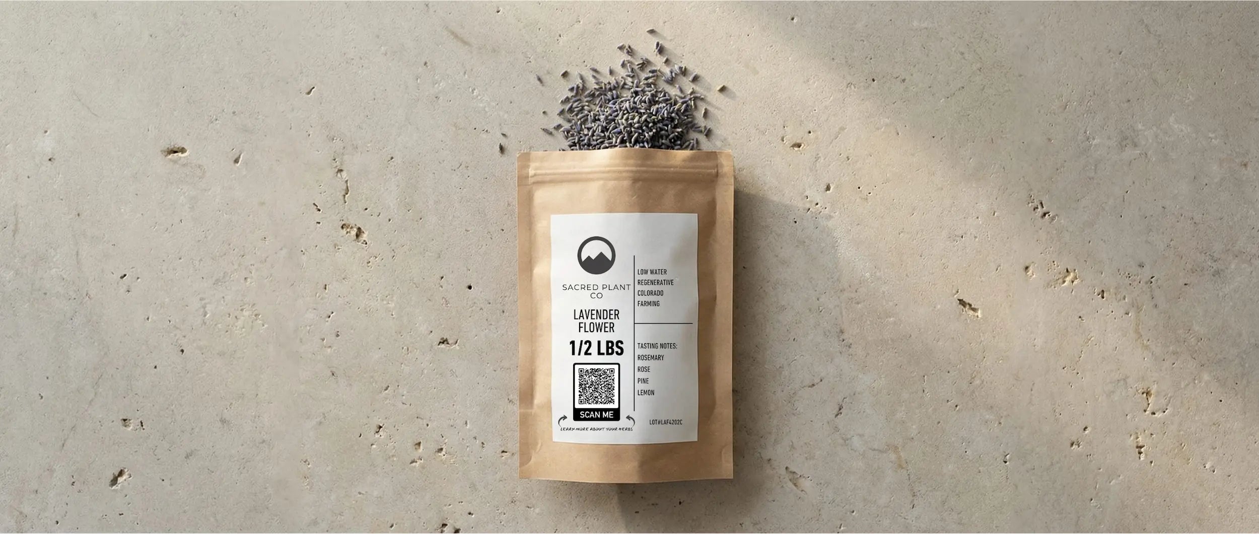 A 1/2 lb bag of Sacred Plant Co regenerative lavender flowers on a stone surface, spilling deep purple buds next to a QR code for batch-specific lab testing.