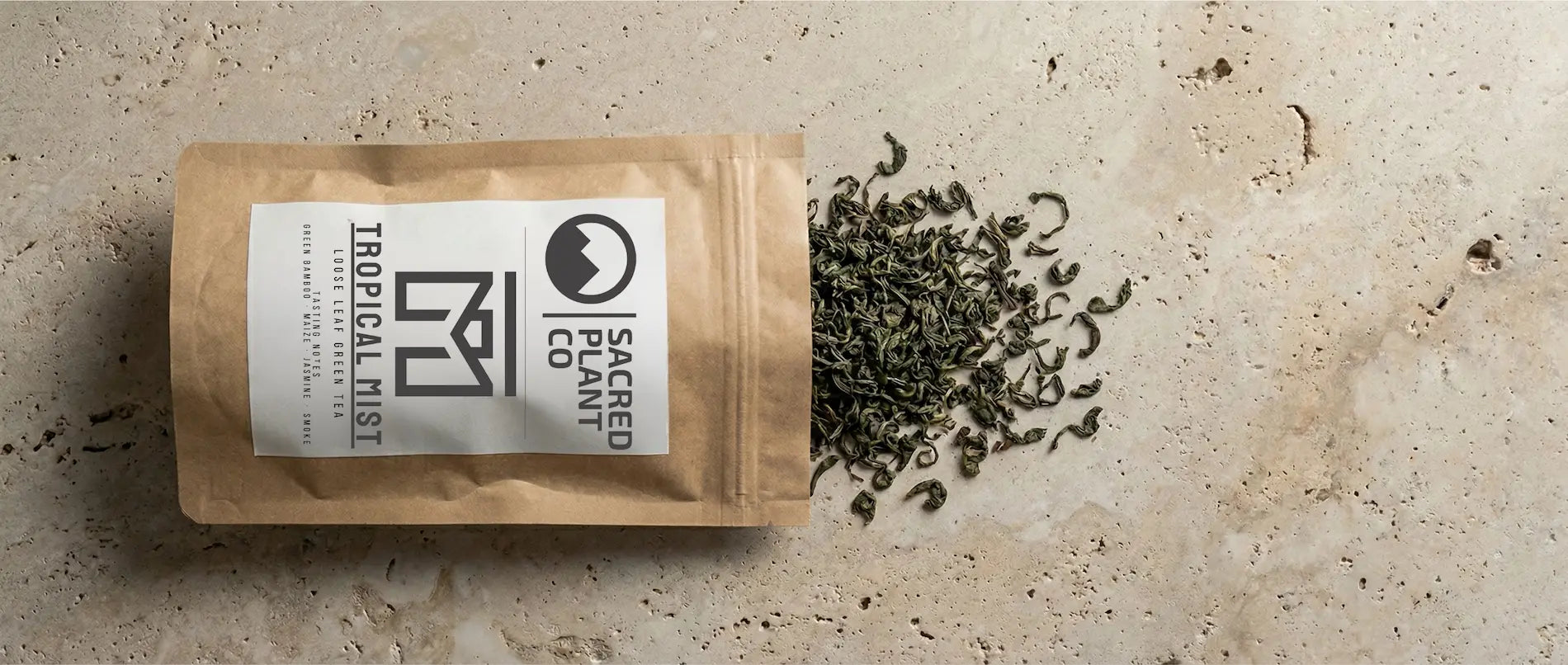 Sacred Plant Co Tropical Mist tea bag spilling dried Chun Mei green tea leaves onto a textured stone surface. features the classic "precious eyebrow" roll of Chun Mei style tea.