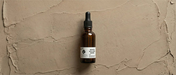Top-down view of Sacred Plant Co White Willow Bark Tincture bottle on a textured natural clay surface.
