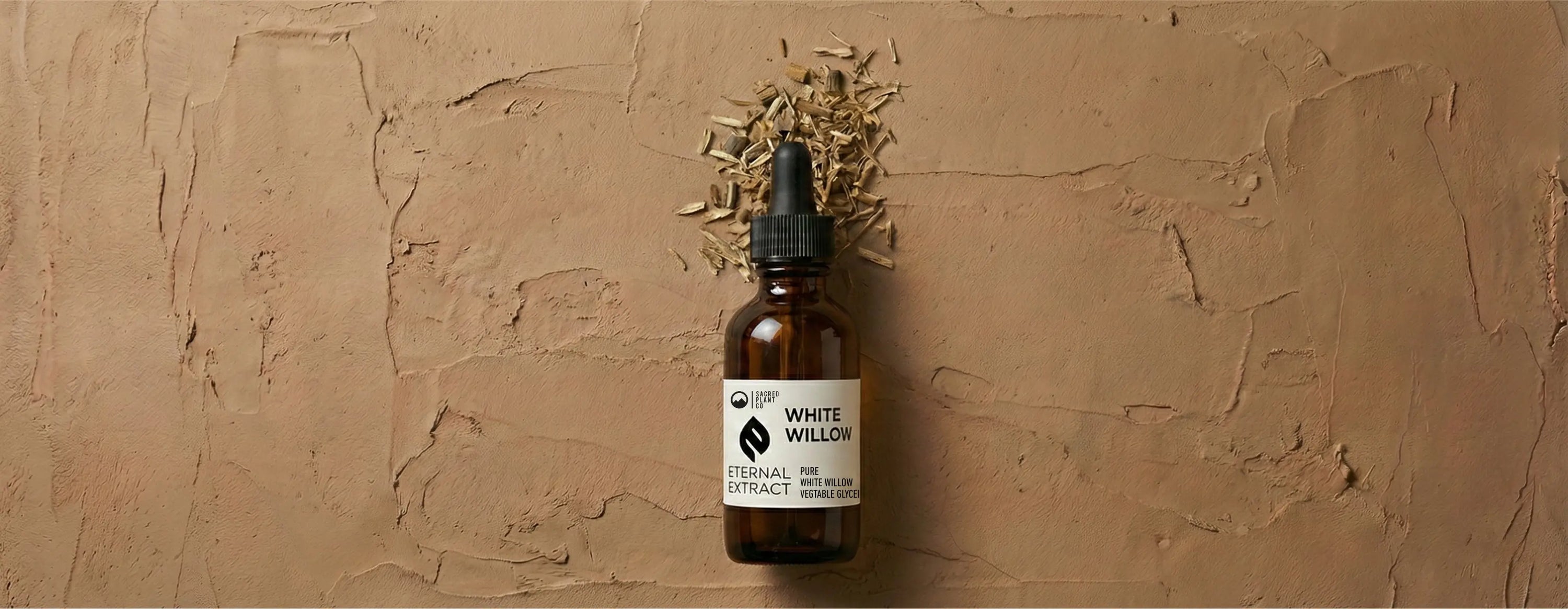 Sacred Plant Co White Willow Bark Tincture Eternal Extract bottle lying flat on a textured clay surface, labeled as pure white willow bark and vegetable glycerin.