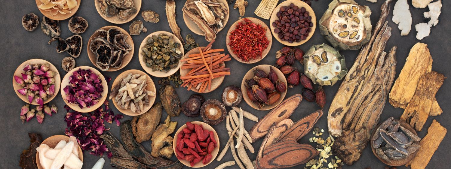 Assorted traditional Chinese medicine herbs displayed in wooden bowls on a dark surface, Includes rose buds, cinnamon, berries, and dried mushrooms, representing holistic health and natural healing ingredients.