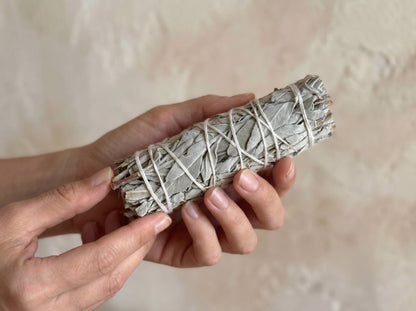 Hand-wrapped 4-inch white sage smudge stick held in hands, showing leaf texture and cotton string