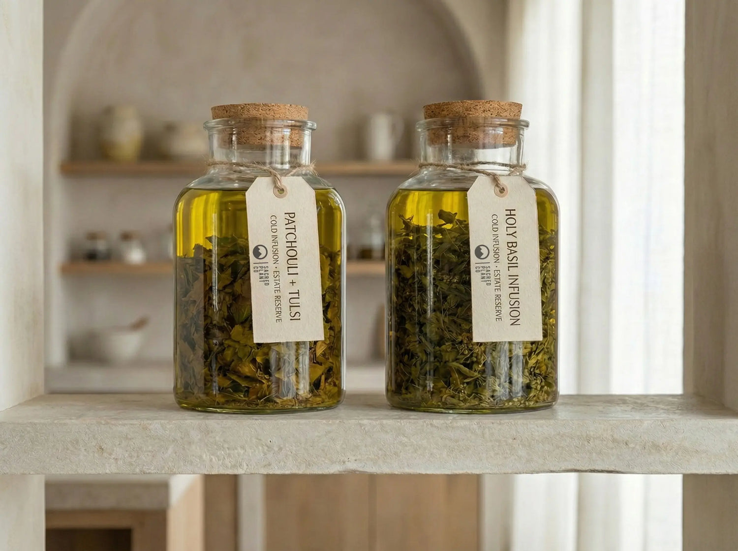 Two glass apothecary jars on a limestone shelf containing a golden cold infusion of whole Patchouli and Tulsi leaves, labeled "Estate Reserve" and steeping in oil.