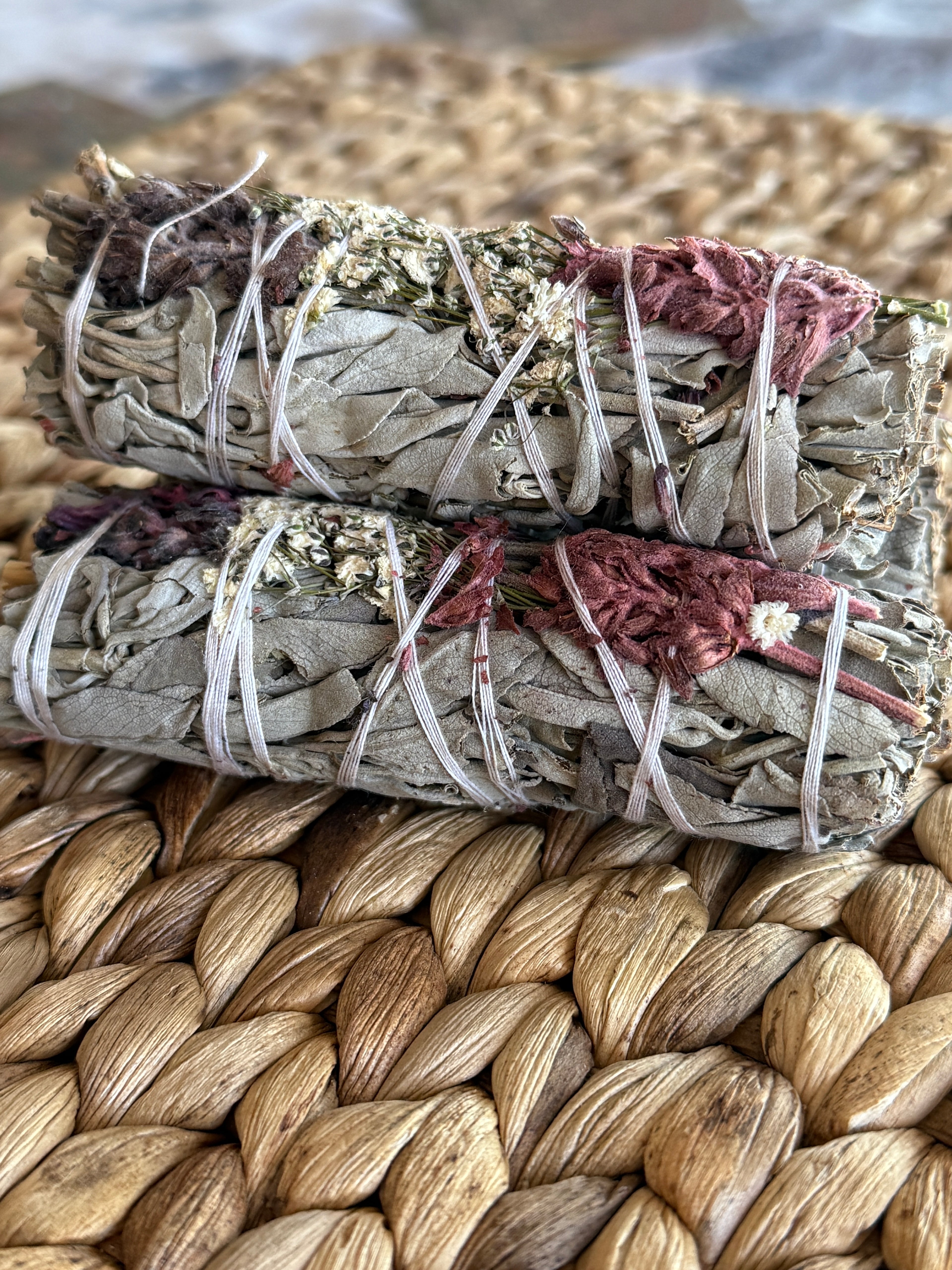 Close-up of consecrated white sage smudge sticks with wildcrafted flowers, tied with natural cotton string for ritual burning.