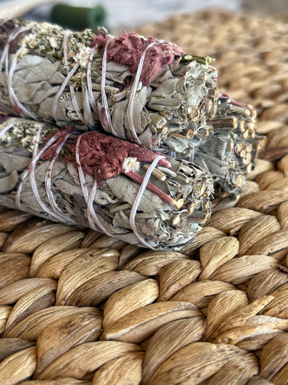 White sage smudge sticks adorned with sacred herbs and blossoms, handcrafted for spiritual purification and ceremonial use.